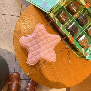 Top view of pink star-shaped quilted crossbody bag with gold chain on wooden table