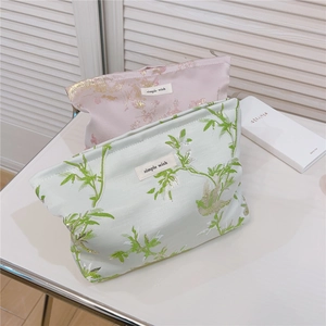 Broderie détaillée d'oiseaux et de fleurs sur une trousse à maquillage en tissu texturé