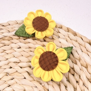 Detail of two handmade sunflower hair clips with yellow ribbon petals on a woven mat