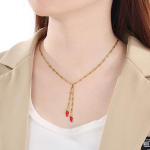 Close-up of a gold chain necklace featuring two red chili pepper charms on a model