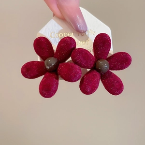 Close-up of dark red flocked flower earrings with velvet texture and copper material