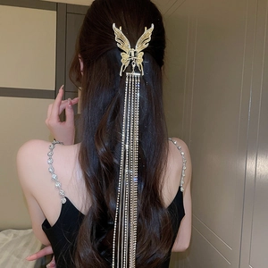 Détail d'une pince à cheveux papillon dorée avec de longs glands et des strass