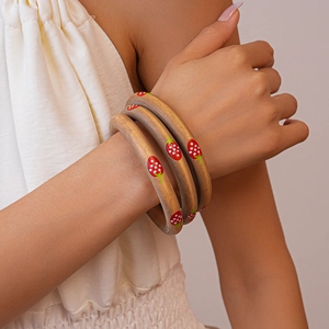 Detailed view of three-piece wooden bracelets with red strawberry prints on a matte gold base