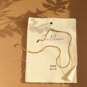 Detailaufnahme einer zweilagigen goldenen Schlangenkette auf einem Stoffbeutel