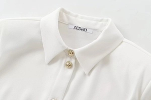 Detail of white crepe shirt collar featuring a gold textured button and sharp lapel