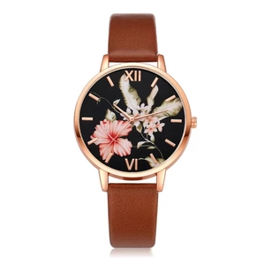 Detail of rose gold watch with floral black dial and brown leather texture strap