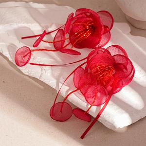 Détail de boucles d'oreilles fleurs en dentelle rouge avec étamines perlées sur fond texturé