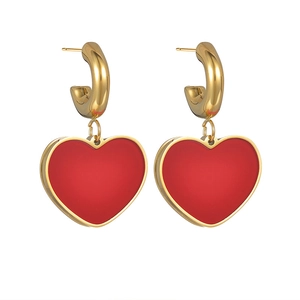 Close-up of golden C-shaped stud earrings with red heart-shaped enamel pendants