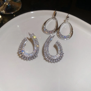 Macro shot of silver zircon water-drop and horseshoe earrings on white ceramic dish