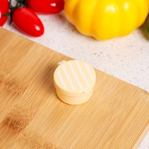 Close-up of a yellow mini round sauce container with striped lid on a wooden board