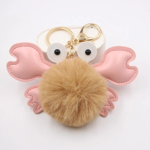 Close-up of pink and brown crab pompom keychain with golden metal ring and soft fur texture