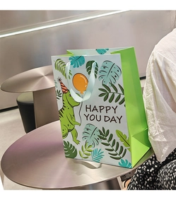 Detail of green cartoon dinosaur gift bag with Happy You Day text on a metal table