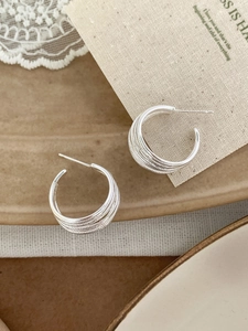Macro detail of layered silver C-shaped hoop earrings with spiral metal texture