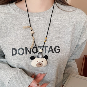 Close-up of cute white bear pendant necklace with plaid hat on grey sweater
