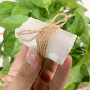 Natural selenite crystal rods bundled with jute rope, held against a soft green background