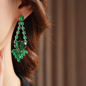 Detailed view of silver heart drop earrings with green zircon stones on model