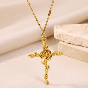 Detail of a gold rose cross necklace displayed on a beige stone prop with a fine chain