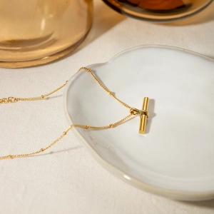 Detail of an 18K gold-plated beaded chain necklace with T-bar pendant on ceramic plate