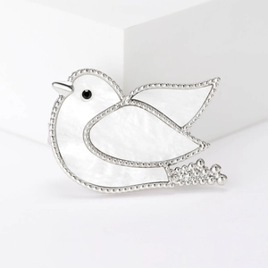 Detailed view of silver bird brooch with white shell inlay on a minimalist background