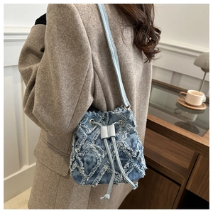 Detail of blue denim bucket bag featuring frayed fringe texture and drawstring closure