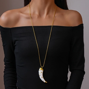 Detail of a white horn pendant on a gold chain worn by a model in black attire