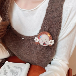 Close-up of a handmade plush girl brooch with floral hair accessories on a knitted sweater