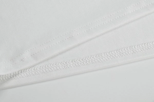 Gros plan sur la double piqûre et la surjeteuse du revers de la robe blanche