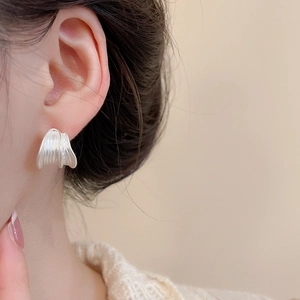 Detail of silver brushed geometric earring with textured pleated design on female ear