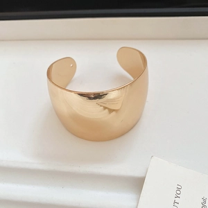 Close-up of a wide polished gold knot cuff bracelet with a glossy mirror finish texture