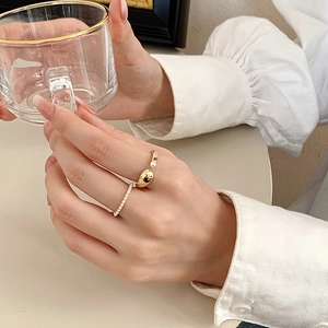 Close-up of gold plated pearl open ring and zircon band worn by a woman holding a glass