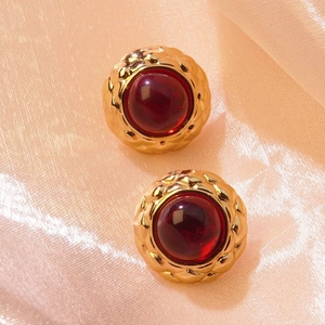 Close-up of vintage gold-plated round earrings with red center and quilted texture