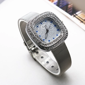 Close-up of silver square watch with crystals, blue markers, and mesh strap