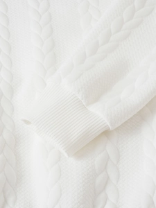 Detailed macro view of white cable knit texture and ribbed cuff on a warm sweater