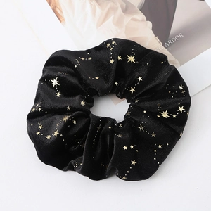Close-up of black velvet scrunchie featuring elegant gold star patterns on a white background