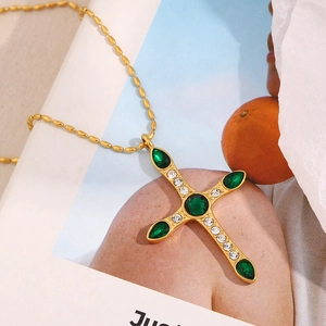 Gros plan du pendentif croix plaqué or 18K avec zircone verte sur une chaîne à billes