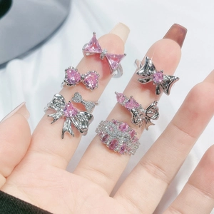 Silver bow rings set with pink zircon stones shown on hand over white silk background