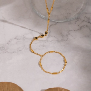 Minimalist 18K gold plated hand chain bracelet with black stones on marble surface