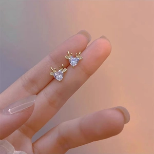 Detail of gold heart-shaped reindeer earrings with clear zircons worn on a finger