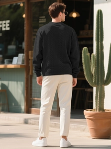 Outdoor back view of men's black cable knit sweater with detailed texture and relaxed fit