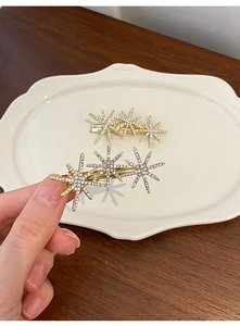 Detailed close-up of two golden star hair clips with sparkling rhinestone inlay design