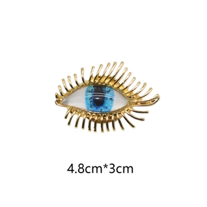 Vintage golden eyelashes blue devil eye brooch measuring 4.8cm by 3cm on white background