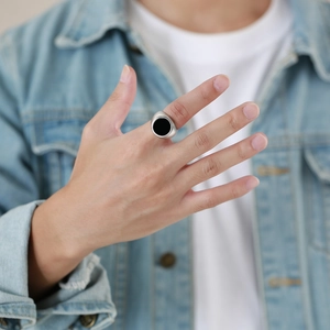 Close-up of a silver men's ring with a black circular inlay worn on a male hand