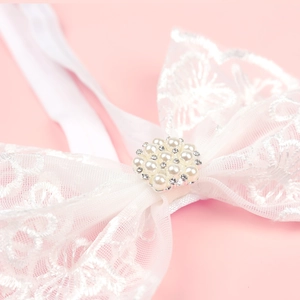 Close-up of white lace bow headband featuring elegant pearl and rhinestone center detailing