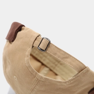 Detail of the adjustable brown leather strap and metal buckle on a khaki canvas cap
