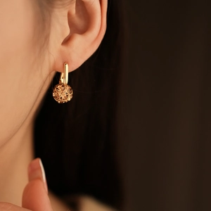 Detailed view of a gold-plated earring featuring a faceted brown spherical charm on model
