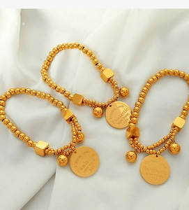 Close-up of 18k gold plated beaded bracelets with engraved round charms on white cloth