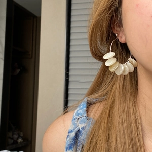 Detail view of silver hoop earrings with pearlescent shell charms worn by a model