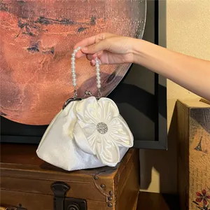 Close-up of white satin handbag with floral detail and elegant pearl top handle