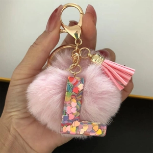 Detail of pink faux fur pom pom and transparent resin letter L with heart sequins