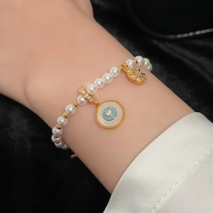 Gros plan d'un bracelet de perles avec breloques dorées et pierre bleue au poignet